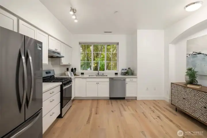 Bright kitchen with white cabinetry, stainless steel appliances, gas range, and hardwood floors.