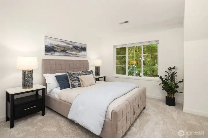 Spacious primary bedroom with wall-to-wall carpet, large window, and peaceful treetop views.