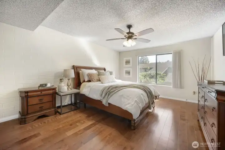 Spacious Primary Bedroom with Ensuite and Generous Closet Space    This inviting primary suite offers a perfect blend of comfort and sophistication. Natural light fills the room, highlighting the warm engineered hardwood floors and soft neutral tones. A large walk-in closet provides ample storage, while the private ensuite bathroom adds convenience and luxury. The space is anchored by a handsome wood-frame bed and complemented by modern touches like a ceiling fan and stylish lighting. Thoughtfully designed for relaxation, this bedroom is a serene retreat at the end of the day.