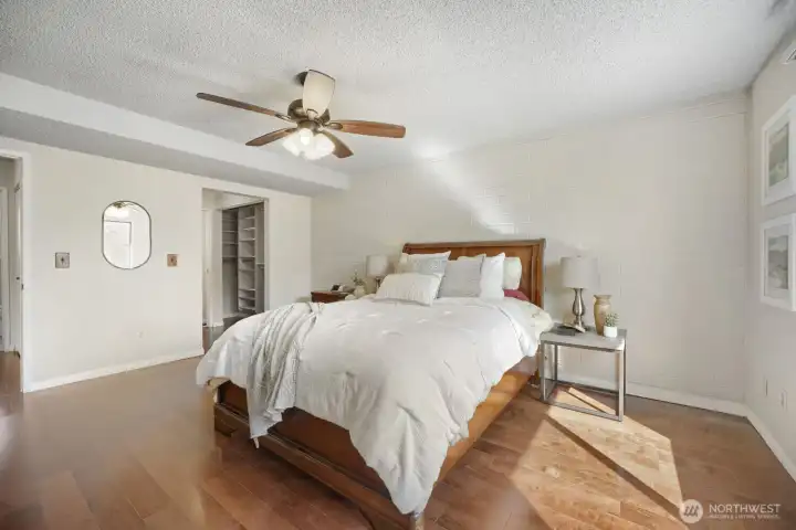 Spacious Primary Bedroom with Ensuite and Generous Closet Space    This inviting primary suite offers a perfect blend of comfort and sophistication. Natural light fills the room, highlighting the warm engineered hardwood floors and soft neutral tones. A large walk-in closet provides ample storage, while the private ensuite bathroom adds convenience and luxury. The space is anchored by a handsome wood-frame bed and complemented by modern touches like a ceiling fan and stylish lighting. Thoughtfully designed for relaxation, this bedroom is a serene retreat at the end of the day.