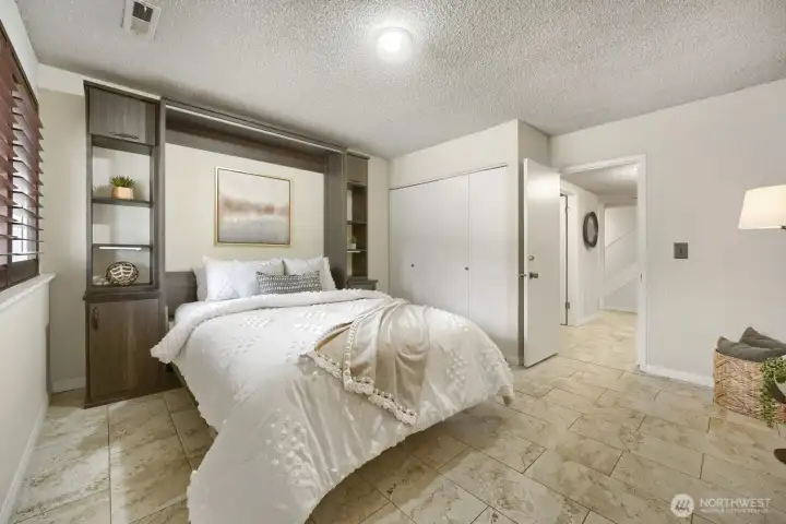 Lower-Level Bedroom with Heated Floors    This beautifully finished lower-level bedroom offers comfort and style with heated tile floors that provide warmth year-round. The space features a neutral palette, textured ceiling, and a large window with wood shutters that fill the room with natural light. Built-in shelving and cabinetry frame the bed, adding both function and elegance. Perfect as a guest suite, home office, or private retreat, this room combines modern convenience with cozy sophistication.