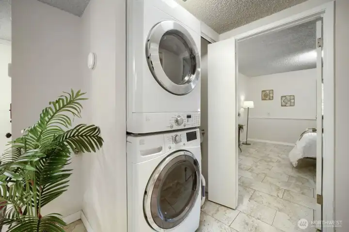 Convenient Laundry Area with Full-Size Washer and Dryer    This well-appointed laundry space features a stacked full-size washer and dryer, offering efficiency and modern convenience. Tucked neatly behind sliding doors, it maximizes functionality while maintaining a clean, streamlined look. Neutral tile flooring and soft lighting create a bright, practical area that connects seamlessly to the adjacent bedroom. Perfect for everyday living, this setup combines style and utility in one compact design.