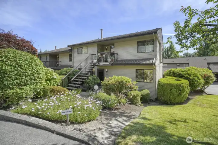 Corner Unit Townhome with Garage    Beautifully maintained corner unit townhome surrounded by lush landscaping and mature greenery. The exterior features a welcoming front entry and a private balcony perfect for relaxing outdoors. Thoughtful design includes a two-car garage and additional parking nearby for convenience. This home offers a sense of privacy and space within a well-kept community, with manicured gardens and tree-lined views enhancing its curb appeal.