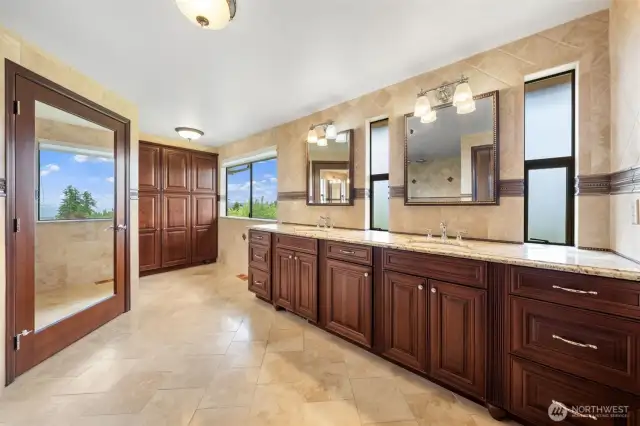 Spacious primary bathroom featuring double sinks, a walk-in shower, walk-in closet, and additional elegant wood cabinetry providing ample storage for all your linens.