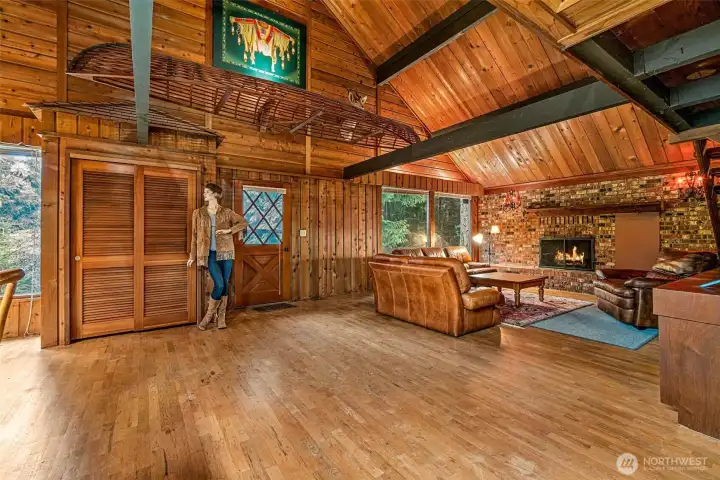 Vaulted cedar ceilings and dark beams draw your eyes up, while hardwood floors ground the space in rustic warmth. A massive brick fireplace wall anchors it all. Quirky details make it unforgettable: a shingled-roof coat closet, a wooden canoe perched above, Native American artwork filtering the light, and yes—Madeline the mannequin keeps her watch from the wall, ready to stay with the house.