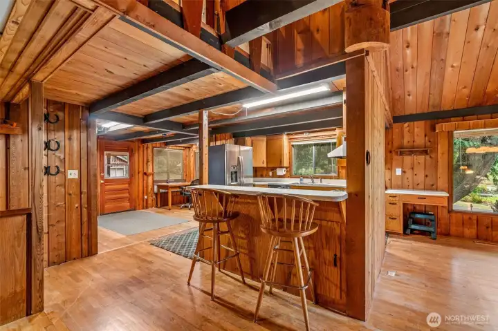 From the great room, the kitchen peeks out like it’s ready to host—bar counter lined up for stories over snacks, a nook that whispers “office… or maybe mischief,” and the front door standing politely by, keeping it all grounded. The spaces tumble into each other with an easy, woodsy charm.