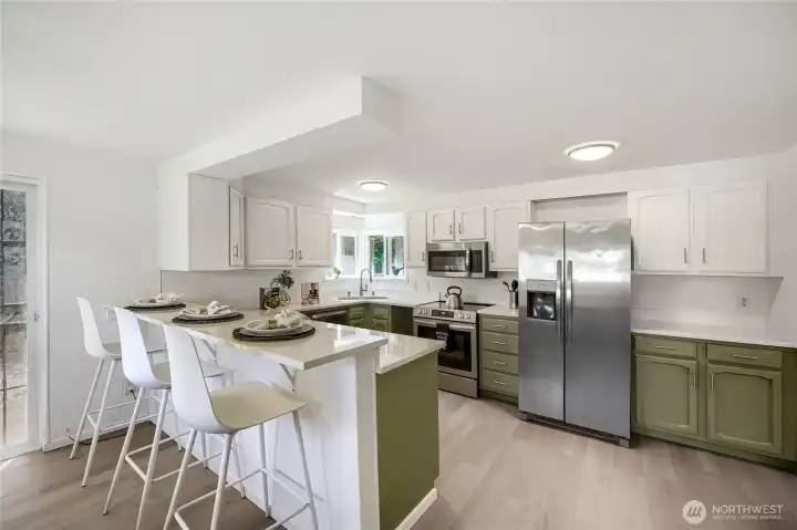 Bright and beautifully updated, this kitchen blends modern style with everyday functionality. Crisp white upper cabinets contrast with olive-green lowers, creating a fresh, designer look. Stainless-steel appliances and sleek white countertops add polish, while the breakfast bar provides a casual spot for dining or conversation. Natural light pours in from multiple windows, enhancing the airy feel and connecting the space seamlessly to the adjacent dining area and patio—perfect for cooking and entertaining alike. Bright and beautifully updated, this kitchen blends modern style with everyday functionality. Crisp white upper cabinets contrast with olive-green lowers, creating a fresh, designer look. Stainless-steel appliances and sleek white countertops add polish, while the breakfast bar provides a casual spot for dining or conversation. Natural light pours in from multiple windows, enhancing the airy feel and connecting the space seamlessly to the adjacent dining area and patio—perfect for cooking and entertaining alike.
