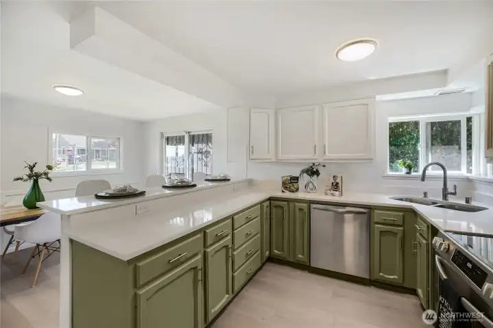 This bright, updated kitchen combines modern style with everyday functionality. Crisp white upper cabinets contrast beautifully with olive-green lowers, complemented by sleek white countertops and stainless-steel appliances. The U-shaped layout offers generous workspace and storage, while the eating bar provides a casual spot for dining or conversation. Sunlight streams through multiple windows, creating an airy, inviting atmosphere that flows effortlessly into the dining area and backyard—perfect for cooking, entertaining, and relaxed Northwest living. This bright, updated kitchen combines modern style with everyday functionality. Crisp white upper cabinets contrast beautifully with olive-green lowers, complemented by sleek white countertops and stainless-steel appliances. The U-shaped layout offers generous workspace and storage, while the eating bar provides a casual spot for dining or conversation. Sunlight streams through multiple windows, creating an airy, inviting atmosphere that flows effortlessly into the dining area and backyard—perfect for cooking, entertaining, and relaxed Northwest living.