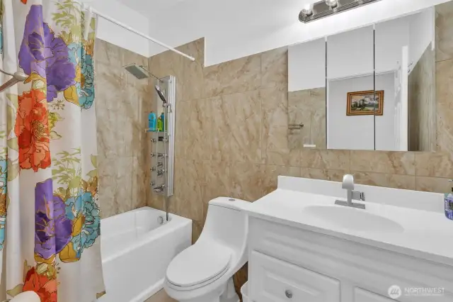 Guest bath has tile floor and tile tub surround. The spa like shower fixture mimics the one in the primary walk in shower. So many settings to chose from for that perfect mix of relaxing spray.