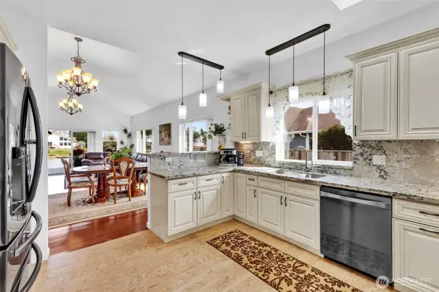 The thoughtfully laid out kitchen with breakfast bar of buffet. You can see the luxury this space affords with slab granite counters, custom cabinetry, stainless steel appliances, designer light fixtures and tile flooring. The kitchen sink overlooks the fenced outdoor garden space.