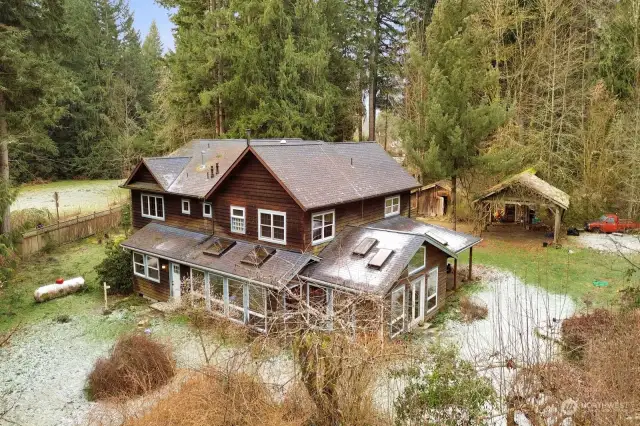 Beautiful farmhouse with low storage barn, carport and wood storage shed behind it.