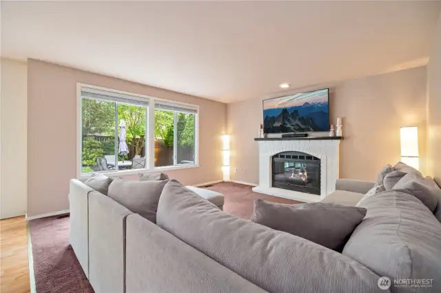 Cozy family room features a white brick fireplace with mantle, large windows, and backyard views—perfect for relaxing or movie nights.