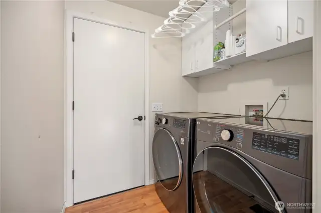 Functional laundry room with front-load washer/dryer, upper cabinets for storage, and hanging rack.