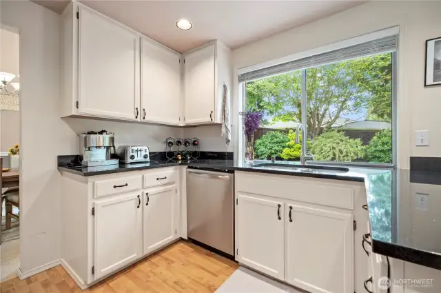 Bright and functional kitchen layout with a picture window over the sink, offering a peaceful view of the lush backyard landscaping.
