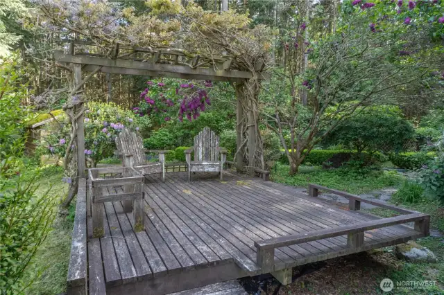 Relax beneath a vine-draped arbor on this charming wood deck—an inviting canvas ready for your personal touch. With a little love, it transforms into a storybook retreat, perfect for morning coffee or evening wine.