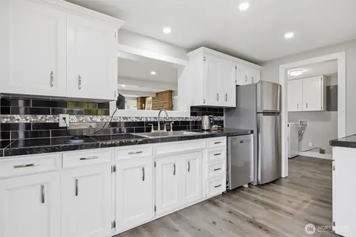 Open kitchen style allows good flow for several people to work together in. Storage and counter space to do prep work on is ample. Clean neutral laminate flooring blends well with the white and black theme, making a easy flow to the look. Open kitchen style allows good flow for several people to work together in. Storage and counter space to do prep work on is ample. Clean neutral laminate flooring blends well with the white and black theme, making a easy flow to the look.