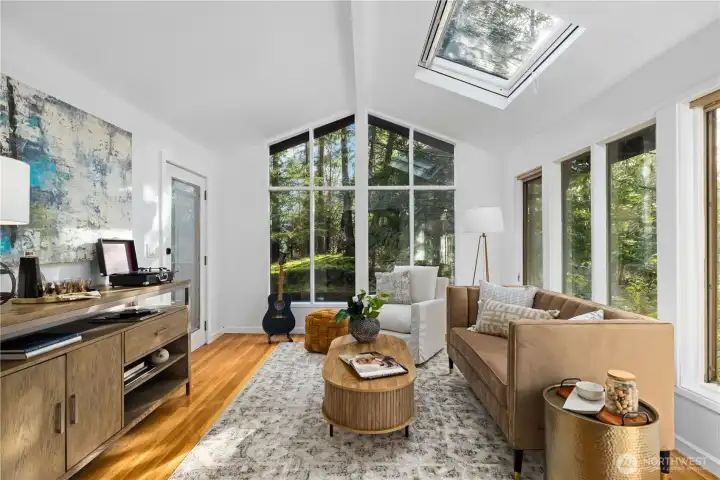 Sunroom with vaulted ceilings, skylight, and walls of glass offers a flexible space for relaxing, working, or simply enjoying the peaceful setting.