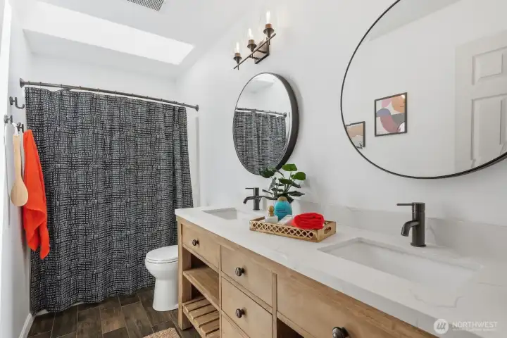 Updated guest full bath featuring a double-sink vanity, new flooring, updated mirrors, and modern fixtures.