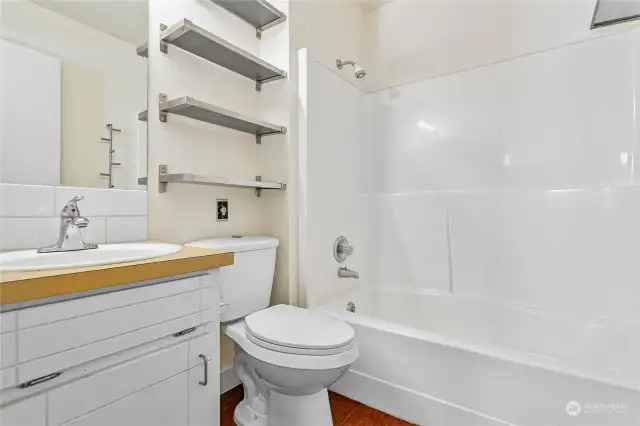 Full bathroom with newer toilet and lots of shelving and storage