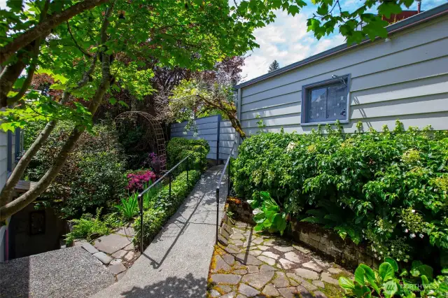 This cozy walkway leads to the garage which is accessed from the alley behind the home. To the left is the pathway to a cozy patio. Flowers and established plantings surround.