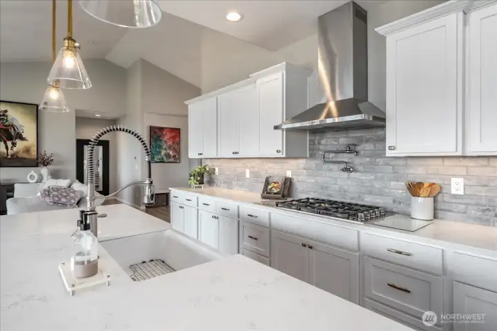 View of kitchen with quartz countertops, stainless appliances, tile backsplash and pot filler.