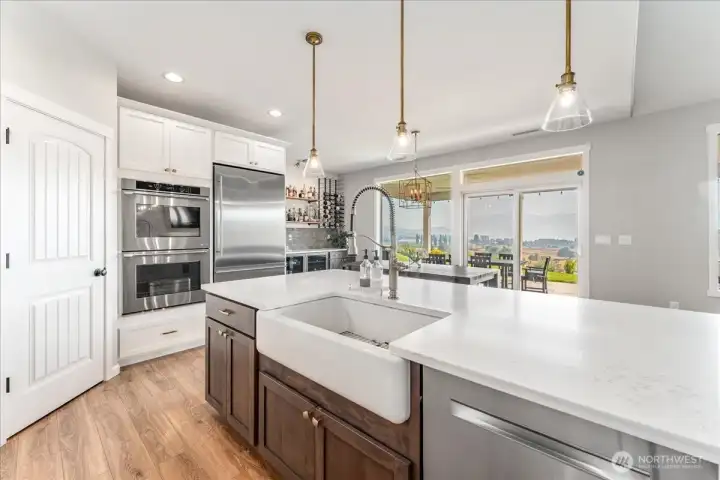 View of kitchen with quartz countertops, pendant lights, farmhouse sink and stainless steel appliances.