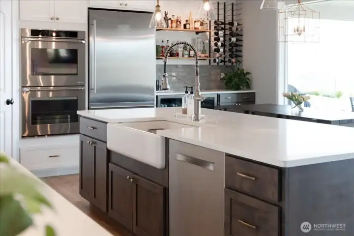 Kitchen with quartz countertops, farmhouse sink, stainless steel appliances and built in bar.