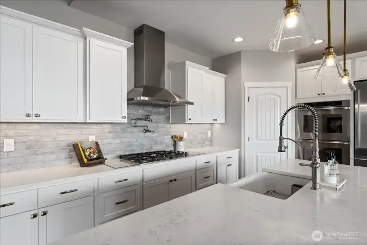 View of kitchen with quartz countertops, pendant lighting, stainless steel appliances and tile backsplash.