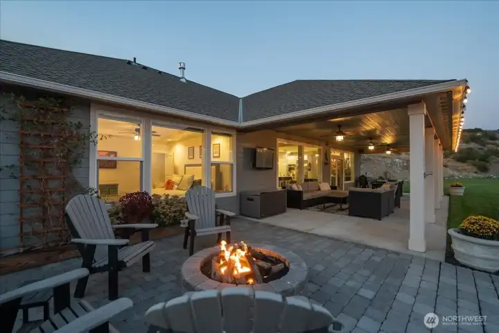 Twilight view of home with outdoor fire pit, lounge, dining and BBQ area with glass sliding doors for seamless indoor-outdoor living.
