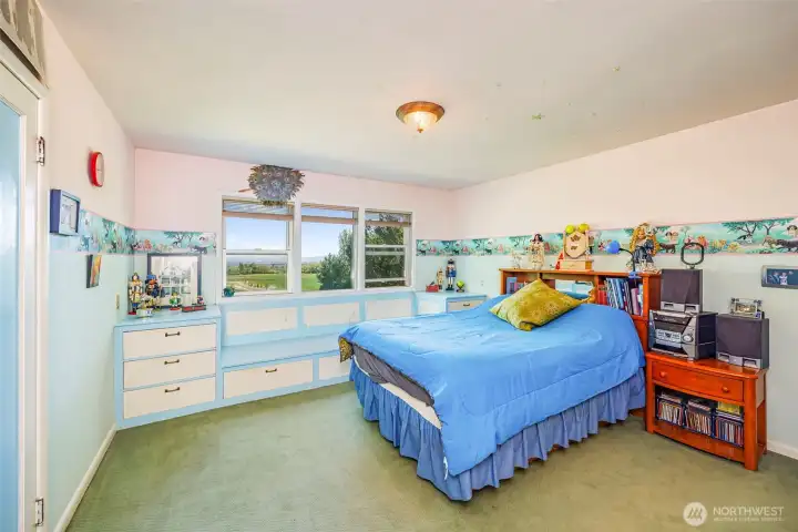 This inviting upstairs bedroom features custom built-ins, a spacious walk-in closet, and a cozy sitting area by the windows, perfect for relaxing and enjoying the view. A perfect blend of comfort, functionality, and style.