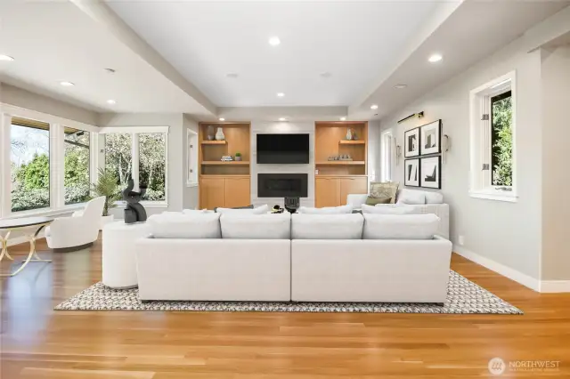 Rich hardwood floors and a stately gas fireplace with a stone surround anchor the space, while custom natural wood shelving adds both function and refined artistry.