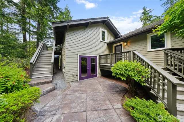 This concrete patio is just outside the workshop (purple door), the mud room to the right, with the loft-level bedroom suite up the stairs to the left.