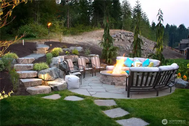 These stone steps lead to the wooded area above this circular patio.