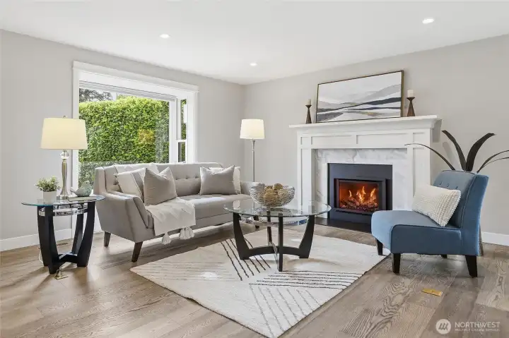 Bright and Inviting Great Room featuring Rich Hardwood Flooring, Recessed Lighting, Expansive Picture Window streaming Natural Light, and an Elegant Thermostatically Controlled Gas Fireplace with Custom White Mantel and Marble Surround creates a Beautiful Focal Point Complemented by Contemporary Finishes and Neutral Tones Ideal for Everyday Living and Entertaining.