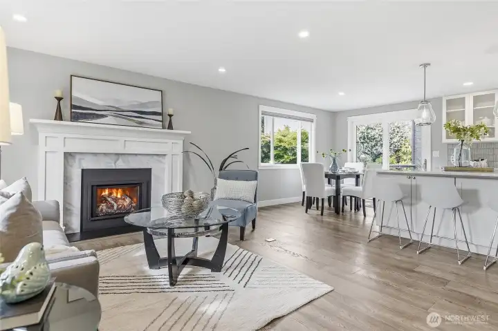 Bright and Inviting Great Room featuring Rich Hardwood Flooring, Recessed Lighting, Expansive Picture Window streaming Natural Light, and an Elegant Thermostatically Controlled Gas Fireplace with Custom White Mantel and Marble Surround creates a Beautiful Focal Point Complemented by Contemporary Finishes and Neutral Tones Ideal for Everyday Living and Entertaining.
