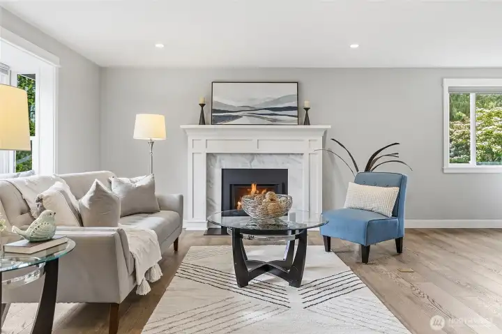 Bright and Inviting Great Room featuring Rich Hardwood Flooring, Recessed Lighting, Expansive Picture Window streaming Natural Light, and an Elegant Thermostatically Controlled Gas Fireplace with Custom White Mantel and Marble Surround creates a Beautiful Focal Point Complemented by Contemporary Finishes and Neutral Tones Ideal for Everyday Living and Entertaining.