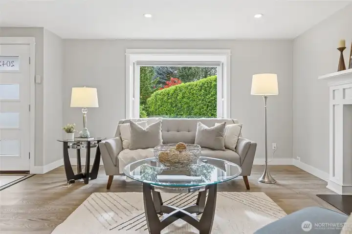 Bright and Inviting Great Room featuring Rich Hardwood Flooring, Recessed Lighting, Expansive Picture Window streaming Natural Light, and an Elegant Thermostatically Controlled Gas Fireplace with Custom White Mantel and Marble Surround creates a Beautiful Focal Point Complemented by Contemporary Finishes and Neutral Tones Ideal for Everyday Living and Entertaining.