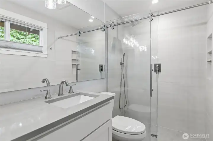 Remodeled Primary Bath with Quartz Vanity, Full-Width Mirror, and a Tiled Walk-in Shower featuring a Frameless Glass Enclosure, Rainfall Shower-head, Built-in Niches, and Contemporary Finishes Throughout.