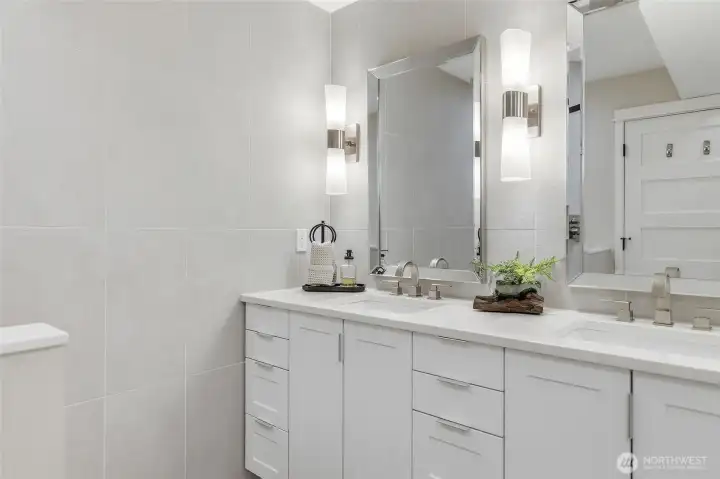 New En-suite Bath featuring a Raised Mirrored Vanity with Quartz Counters, Double Sinks, Designer Lighting, Heated Tile Floors, and Stacked Washer and Dryer.