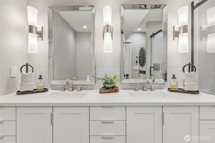 New En-suite Bath featuring a Raised Mirrored Vanity with Quartz Counters, Double Sinks, Designer Lighting, Heated Tile Floors, and Stacked Washer and Dryer.