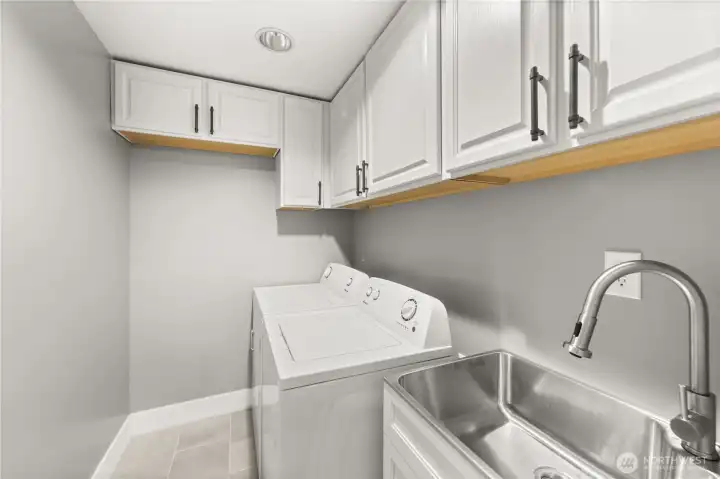 Laundry room equipped with washer, dryer, utility sink, and many overhead cupboards for storage.