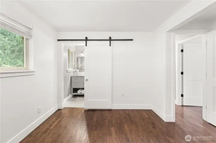 Primary bedroom with sliding barn door leading to the bathroom and adjacent hallway access.