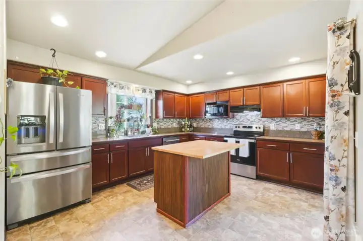 Kitchen with wrap around cabinets, prep island with overhang for counter sitting, full height backsplash, and a view from the kitchen sink.