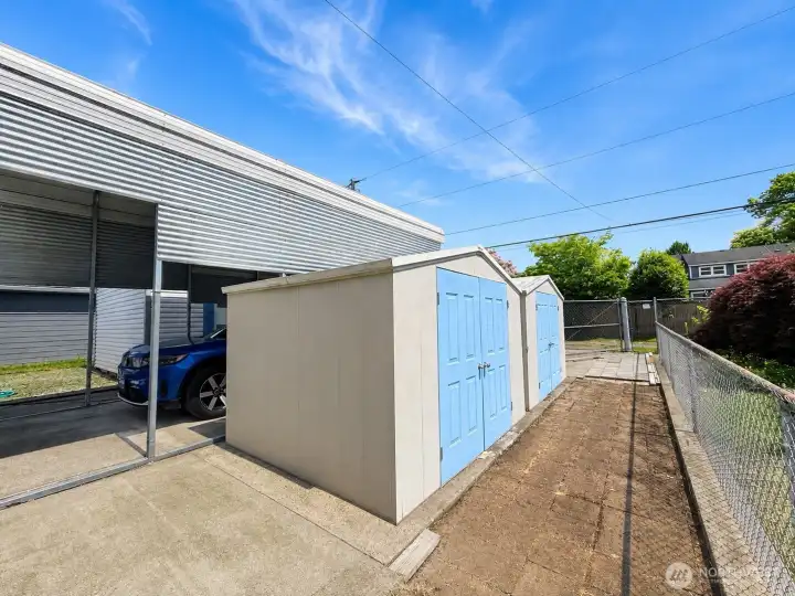 Two sheds in fenced backyard with large gates.