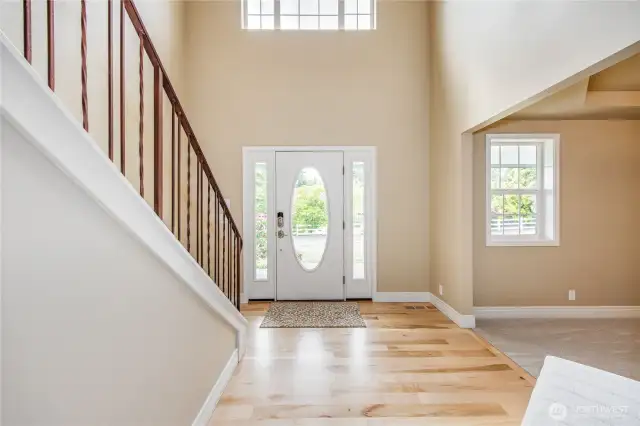 Light-filled foyer with soaring ceilings and open staircase.  To the right is a formal dining room