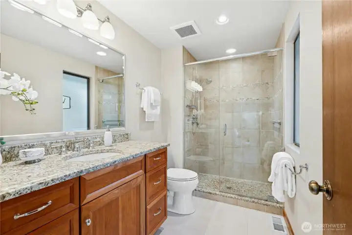 Updated primary bathroom with granite counters, modern fixtures, and elegant tile shower.