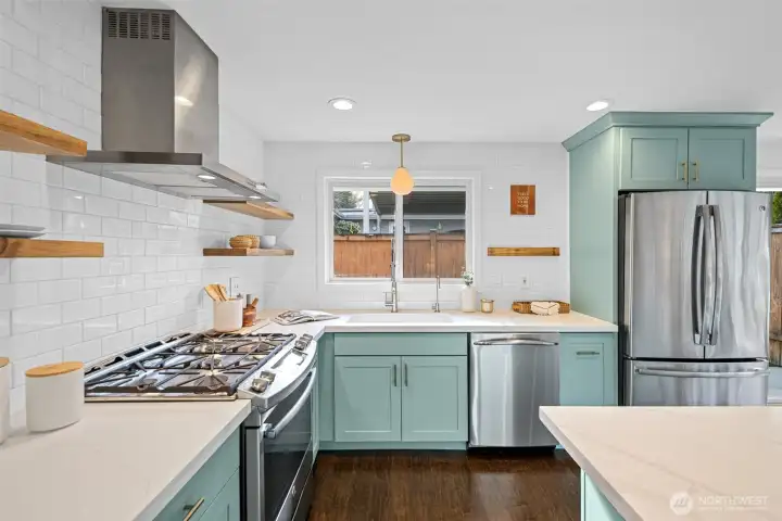 This bright, inviting kitchen is anchored by a GE stainless-steel French-door refrigerator with a spacious bottom freezer, an ergonomic setup that keeps everyday items at eye level and larger storage easily accessible below. Smooth quartz countertops, added during the 2014 kitchen renovation, wrap the workspace beautifully, offering a clean, durable surface for cooking and entertaining.    A Bosch stainless-steel dishwasher sits just below the oversized kitchen window, making clean-up efficient. Above the sink, a warm, sculptural pendant light, part of the 2014 remodel, adds a soft, stylish touch and gently illuminates the workspace. That large window floods the entire area with natural light, creating a warm, cheerful atmosphere that makes the kitchen a pleasure to be in throughout the day.