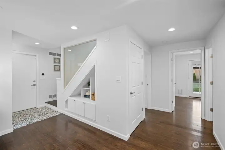 A perfect transition space between the main living areas and the two main-floor bedrooms, this view of the main hallway showcases the lovely tiled entry at the foyer, and beautiful glass wall along the stairwell, which brings more light into the stairwell making it feel open and airy.  The current owner thoughtfully added a pantry beneath the stairs, providing extra storage. Cubby holes under the stairs proved a place for shoes or decor.  The hallway leads to the two main-floor bedrooms and bathroom.