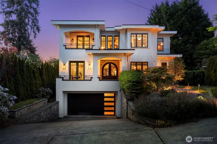 Front of house: Striking three-story exterior with warm interior lighting and lush landscaping at twilight.
