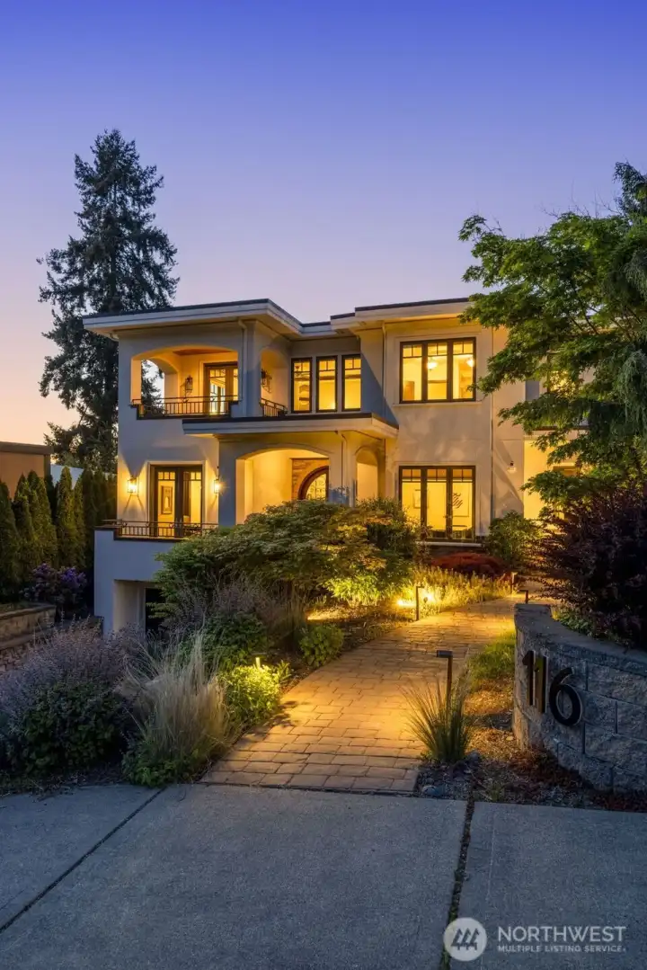 Front photo: Warm evening view of the home's grand entry and architectural detailing, illuminated against the Pacific Northwest sky.